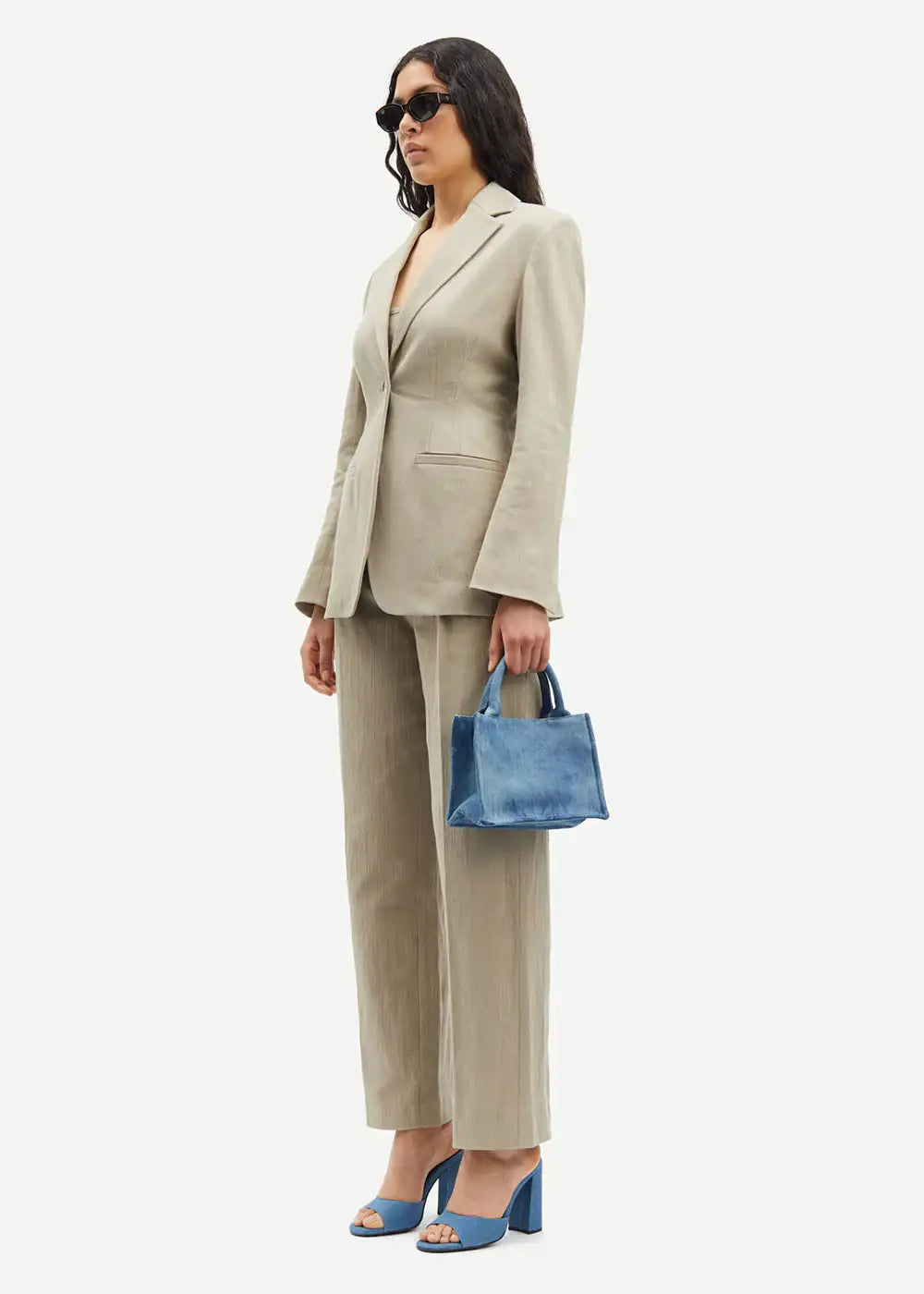Woman in beige linen suit with blue denim handbag and matching heels, wearing sunglasses