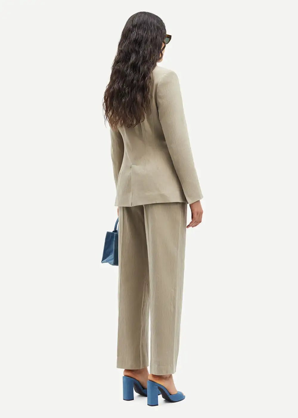 Woman in beige suit with wide-leg trousers, blue heels, and a blue handbag, rear view