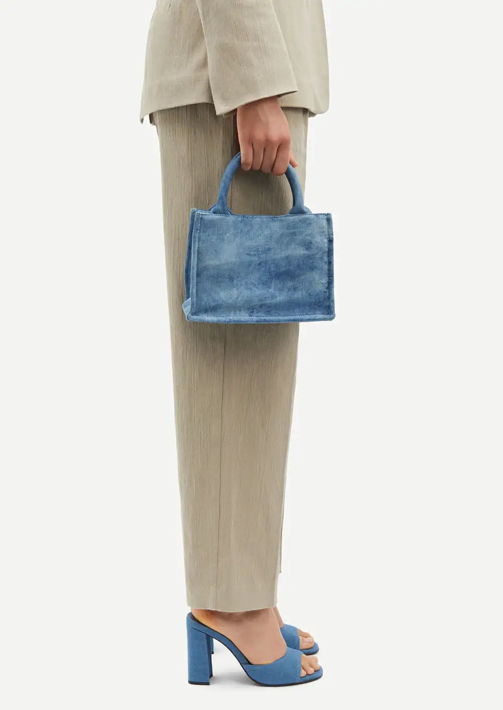 Woman in beige suit holds blue denim mini handbag, wearing matching blue block heel sandals