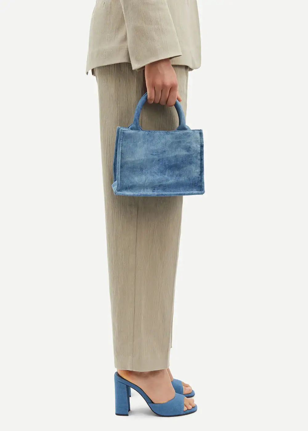 Woman in beige suit holds blue denim mini handbag, wearing matching blue block heel sandals