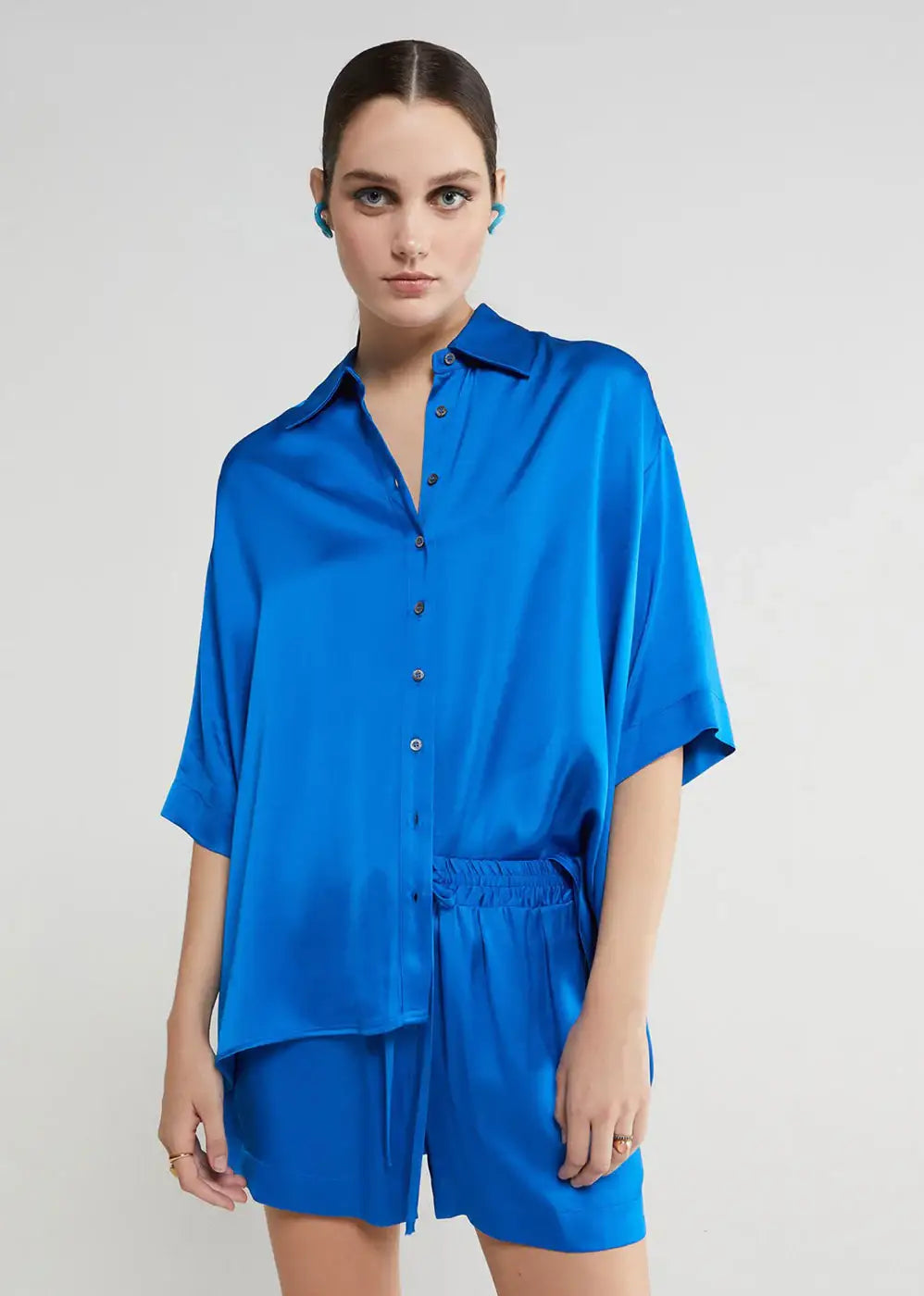 Woman wearing loose blue satin button-up shirt and matching shorts fashion set