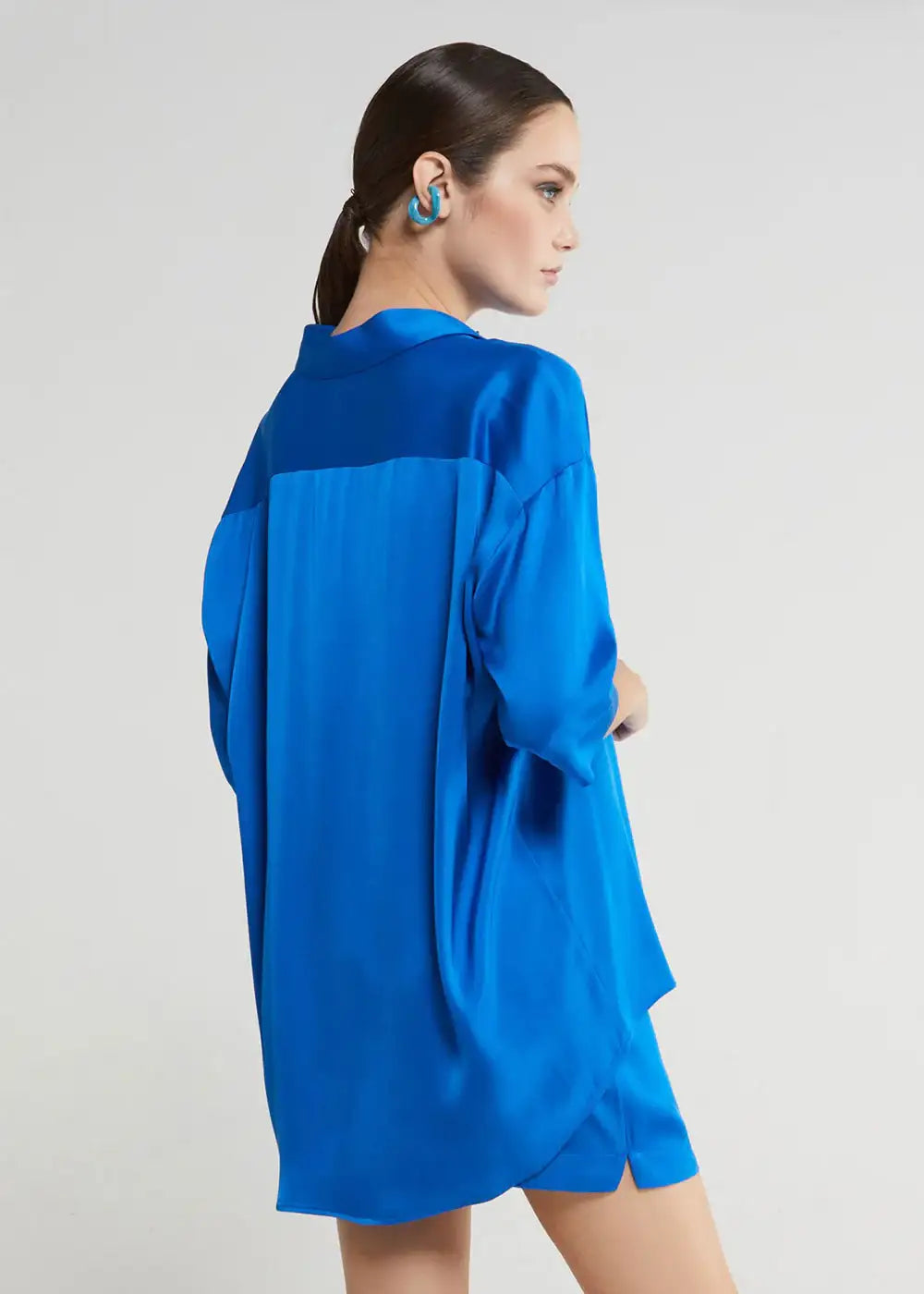 Woman wearing an oversized cobalt blue satin shirt and matching shorts, side profile