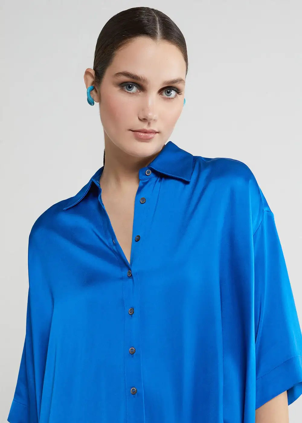 Woman wearing oversized cobalt blue satin shirt with button-up front and pointed collar