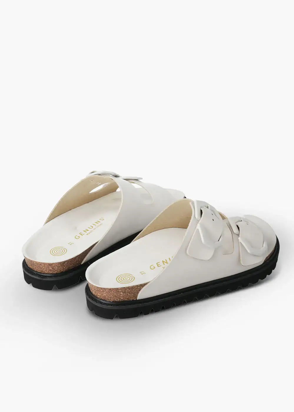 Pair of white slip-on sandals with double buckle straps, cork footbed, and black sole