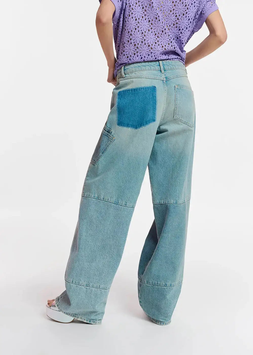 Wide-leg patchwork jeans with contrast blue back pocket, paired with a purple eyelet shirt.