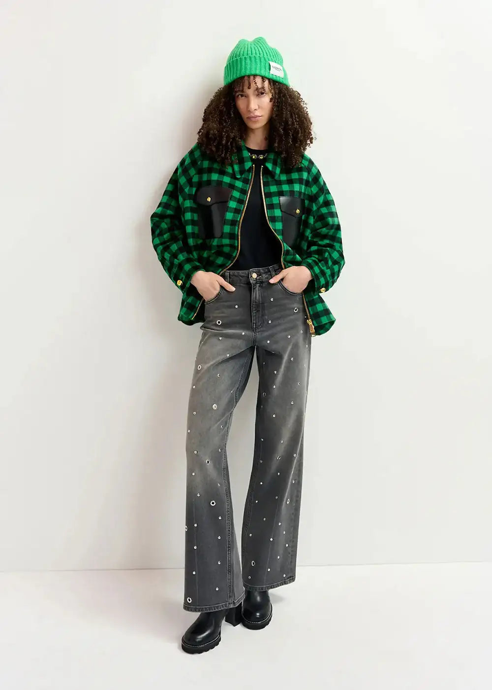 Woman in a green check jacket, grey embellished jeans, green beanie, and black boots.