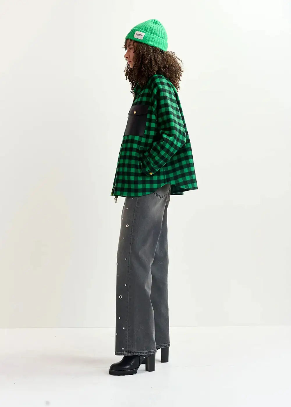 Woman in green checked flannel jacket, green beanie, grey wide-leg jeans, black boots