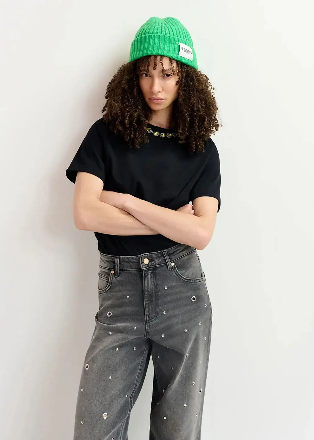 Woman wearing green beanie, black embellished t-shirt, and studded wide-leg grey jeans