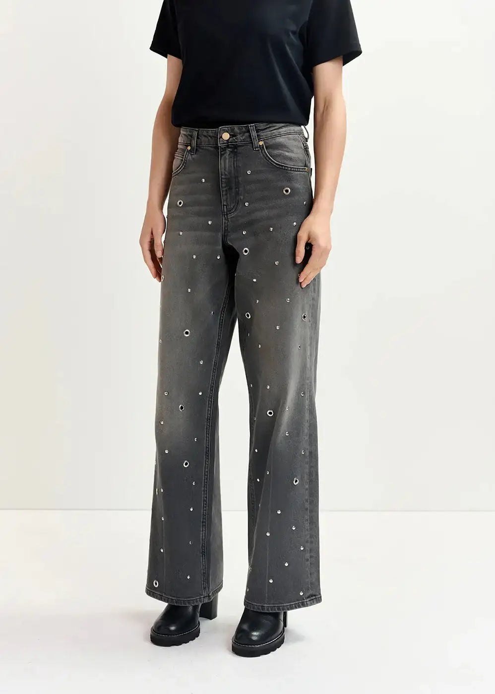 Woman wearing black wide-leg jeans with silver eyelet details and black boots