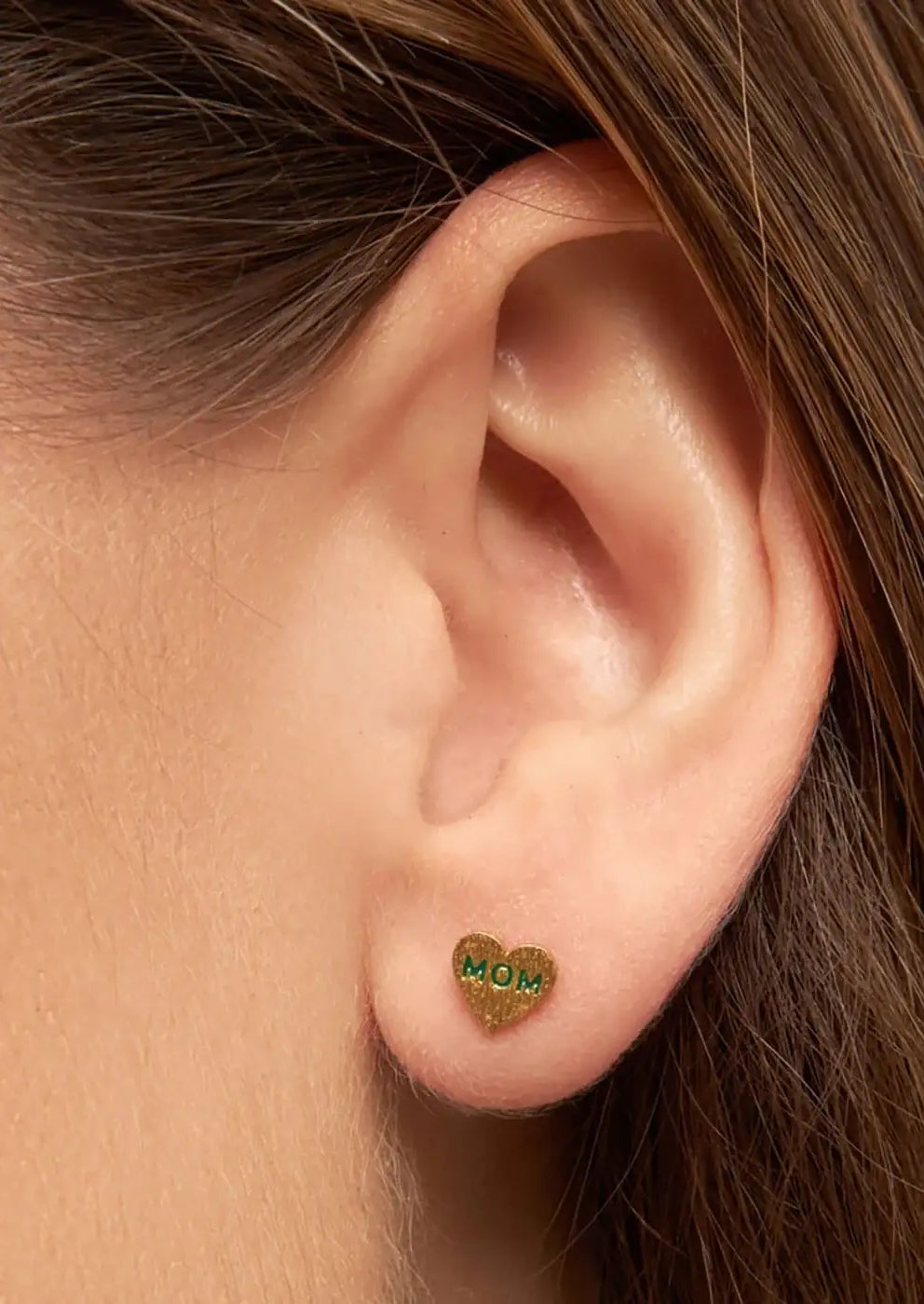 Gold heart-shaped stud earring with green 'MOM' text on earlobe