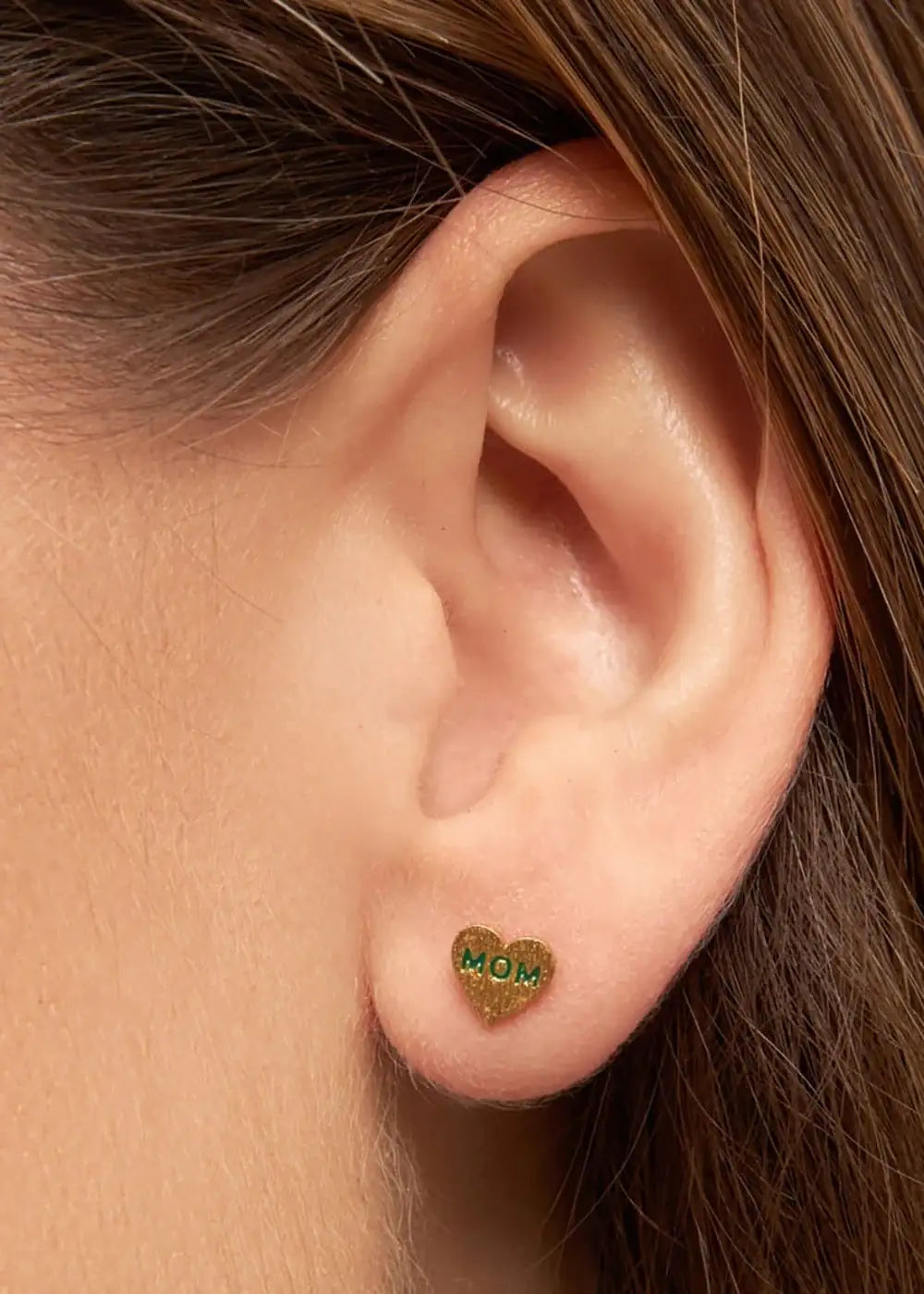 Gold heart-shaped stud earring with green 'MOM' text on earlobe