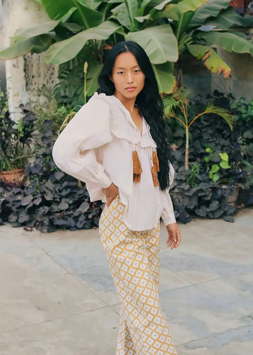 Woman wearing ruffle blouse and patterned wide-leg trousers in tropical garden
