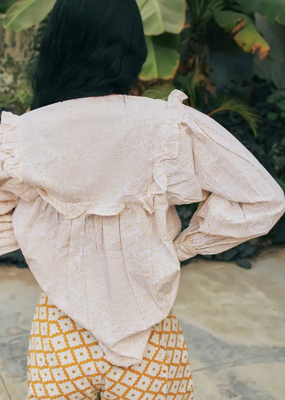 Woman wearing a ruffled floral blouse and geometric patterned trousers outdoors