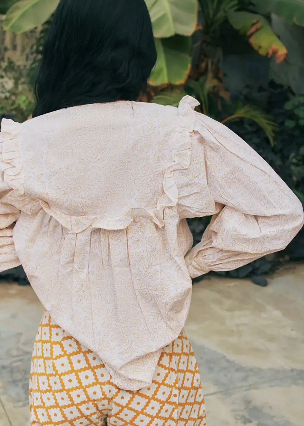 Woman wearing a ruffled floral blouse and geometric patterned trousers outdoors