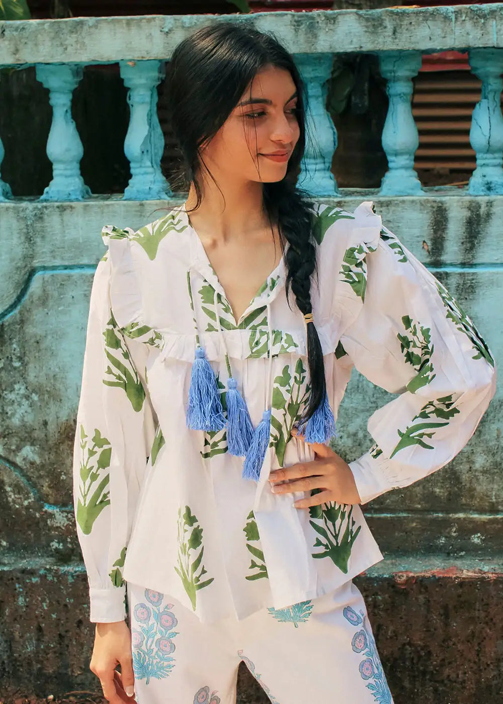 Woman wearing a white blouse with green floral print and blue tassel accents outdoors