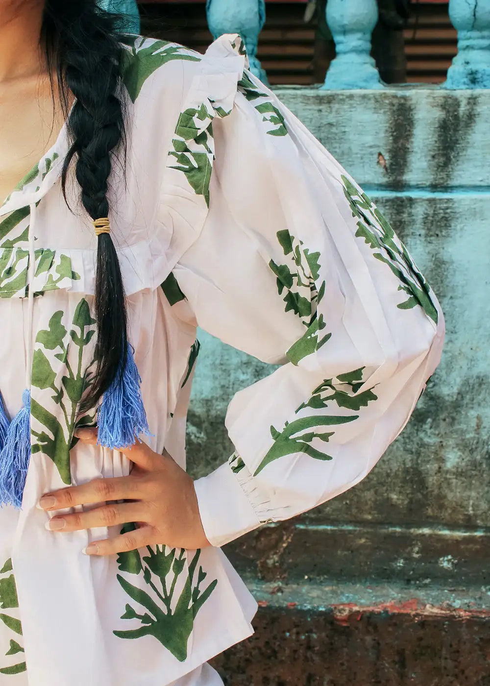 Woman wearing a white blouse with green leafy print, blue tassels, and ruffle details