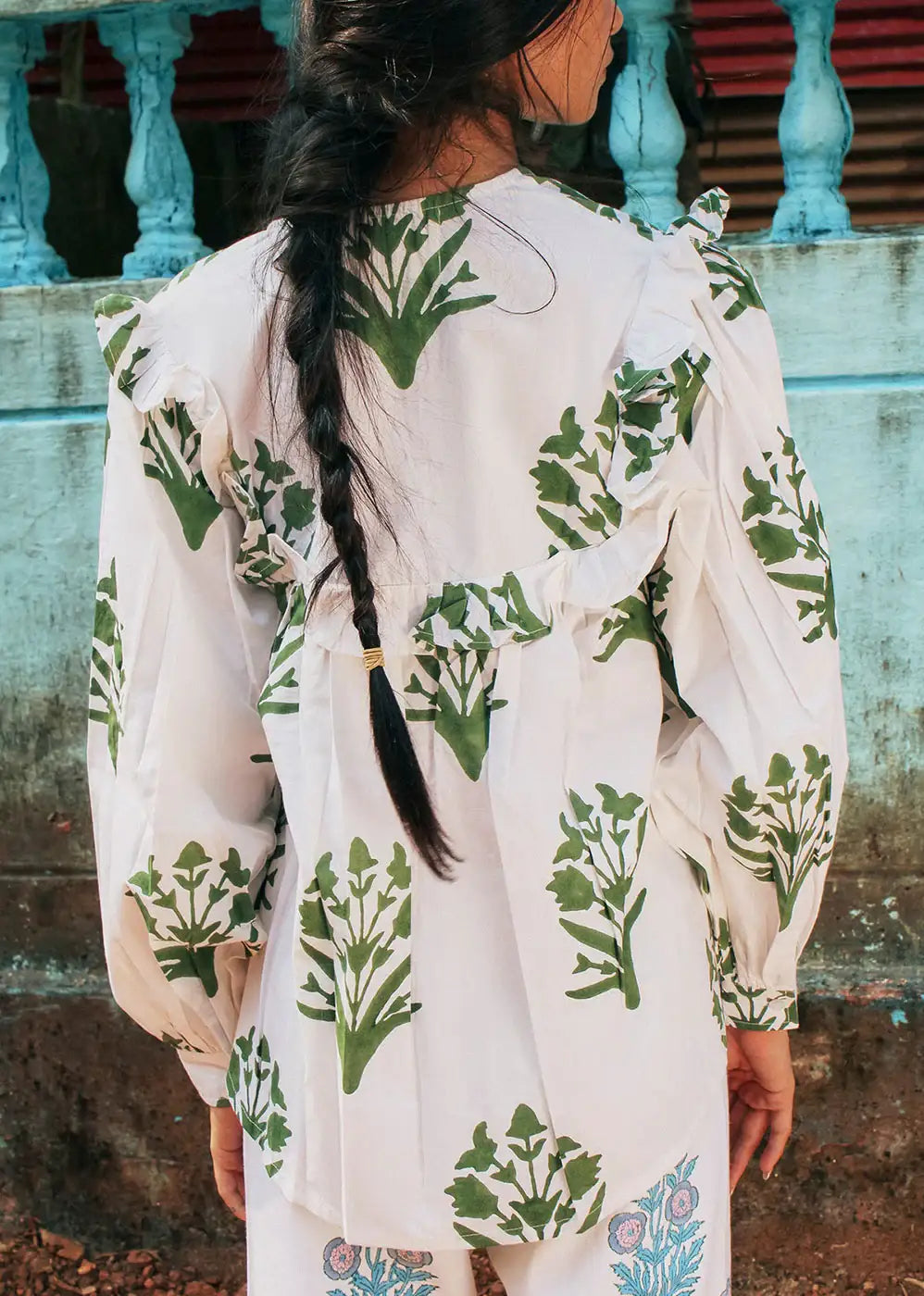 Woman with braid wearing white blouse with green botanical print and ruffle details