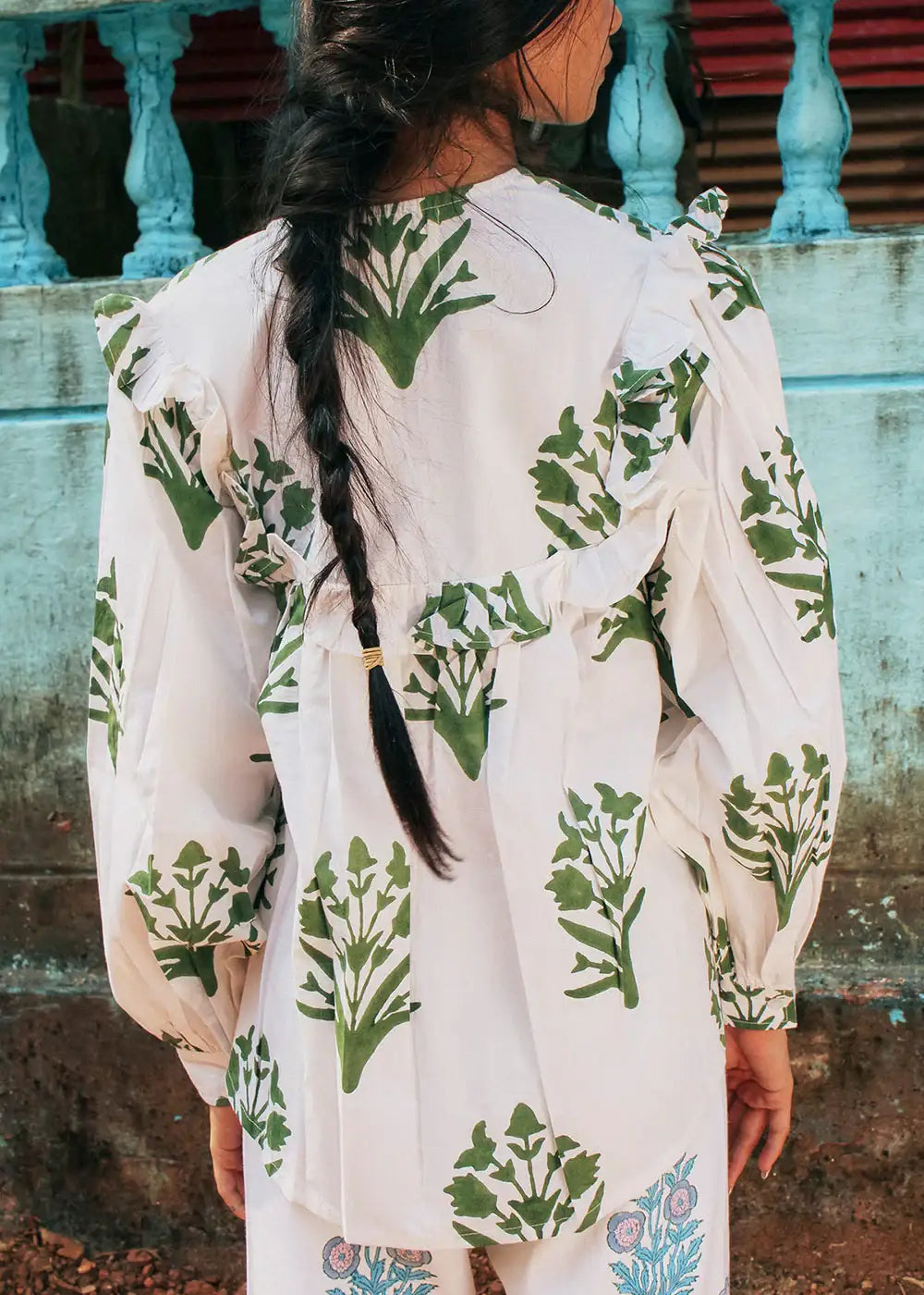 Woman with braid wearing white blouse with green botanical print and ruffle details