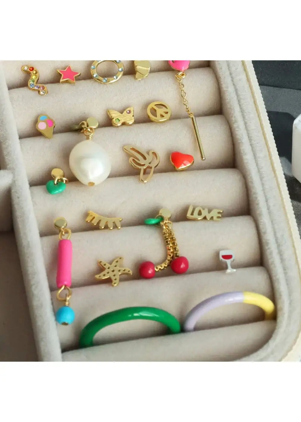Assorted colorful gold plated stud earrings and rings in a beige jewelry organizer