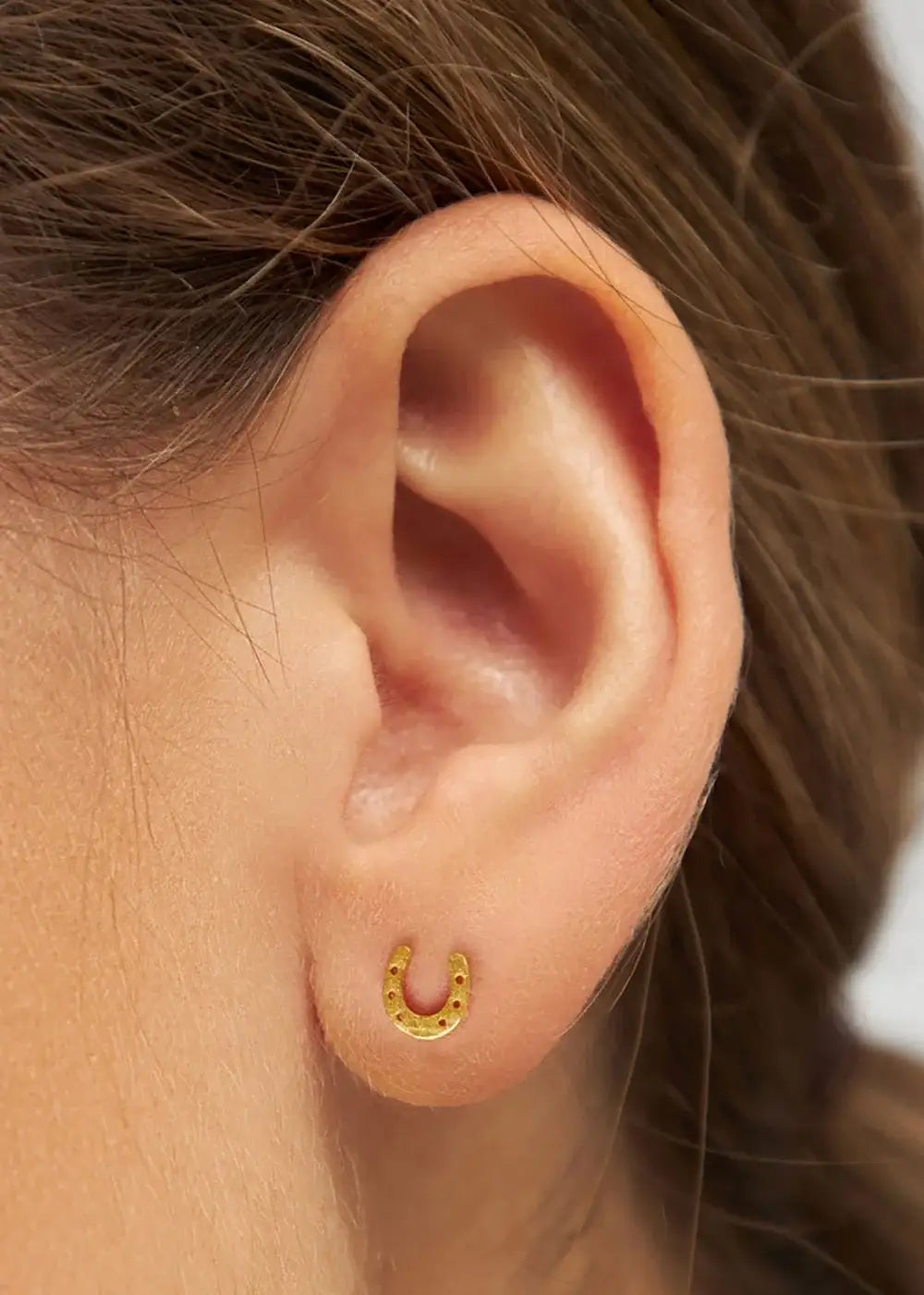 Gold plated horseshoe stud earring worn in pierced ear, close-up jewelry photo