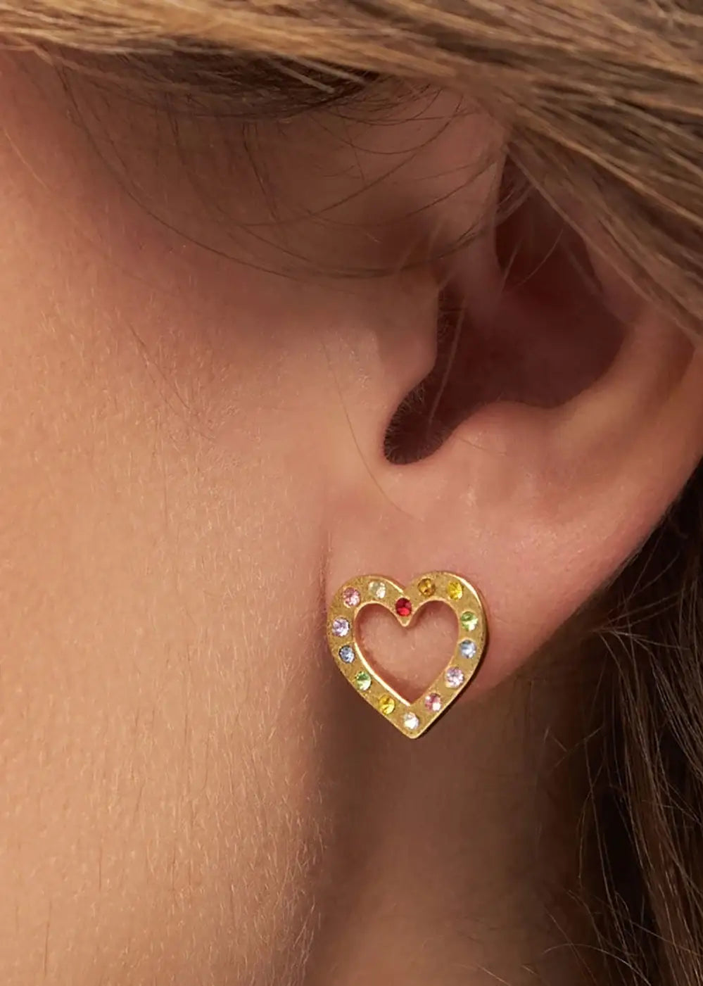 Gold heart-shaped ear stud with rainbow gemstones on ear, fashion jewelry close-up