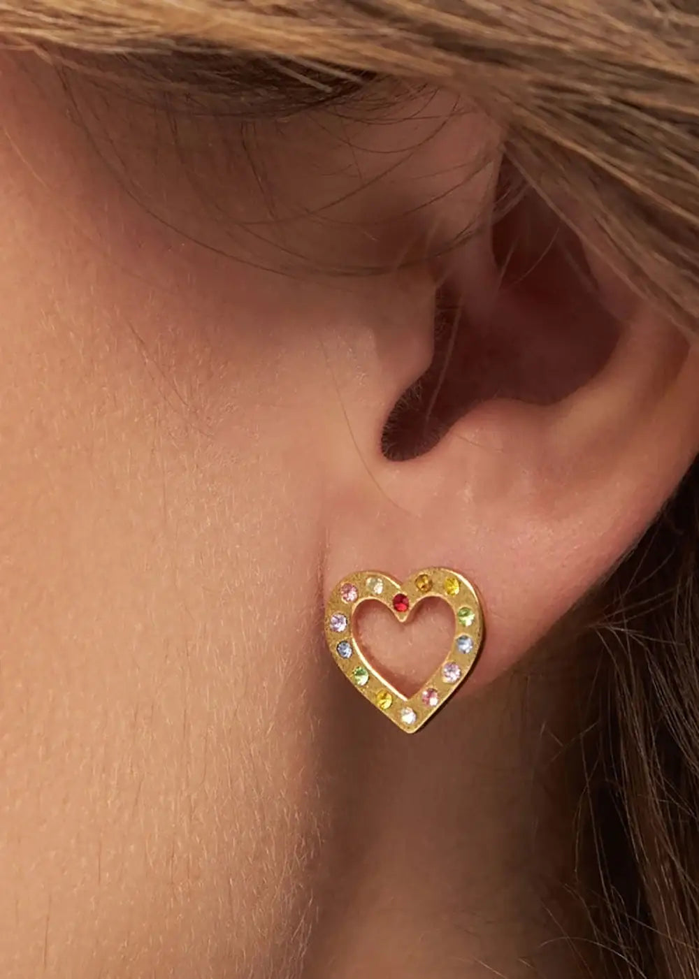 Gold heart-shaped ear stud with rainbow gemstones on ear, fashion jewelry close-up