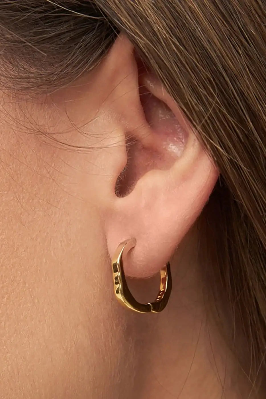 Close-up of a gold plated textured hoop earring worn on a person's ear