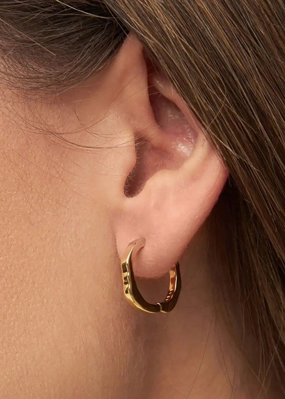 Close-up of a gold plated textured hoop earring worn on a person's ear