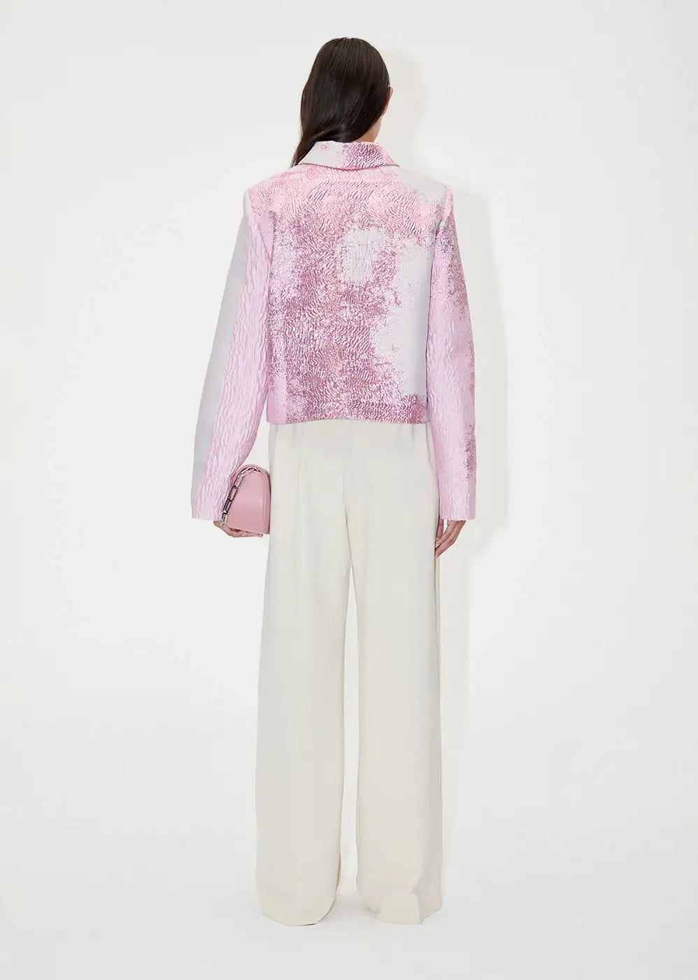 Woman wearing ivory wide-leg pants and textured pink jacket, holding pink handbag, back view