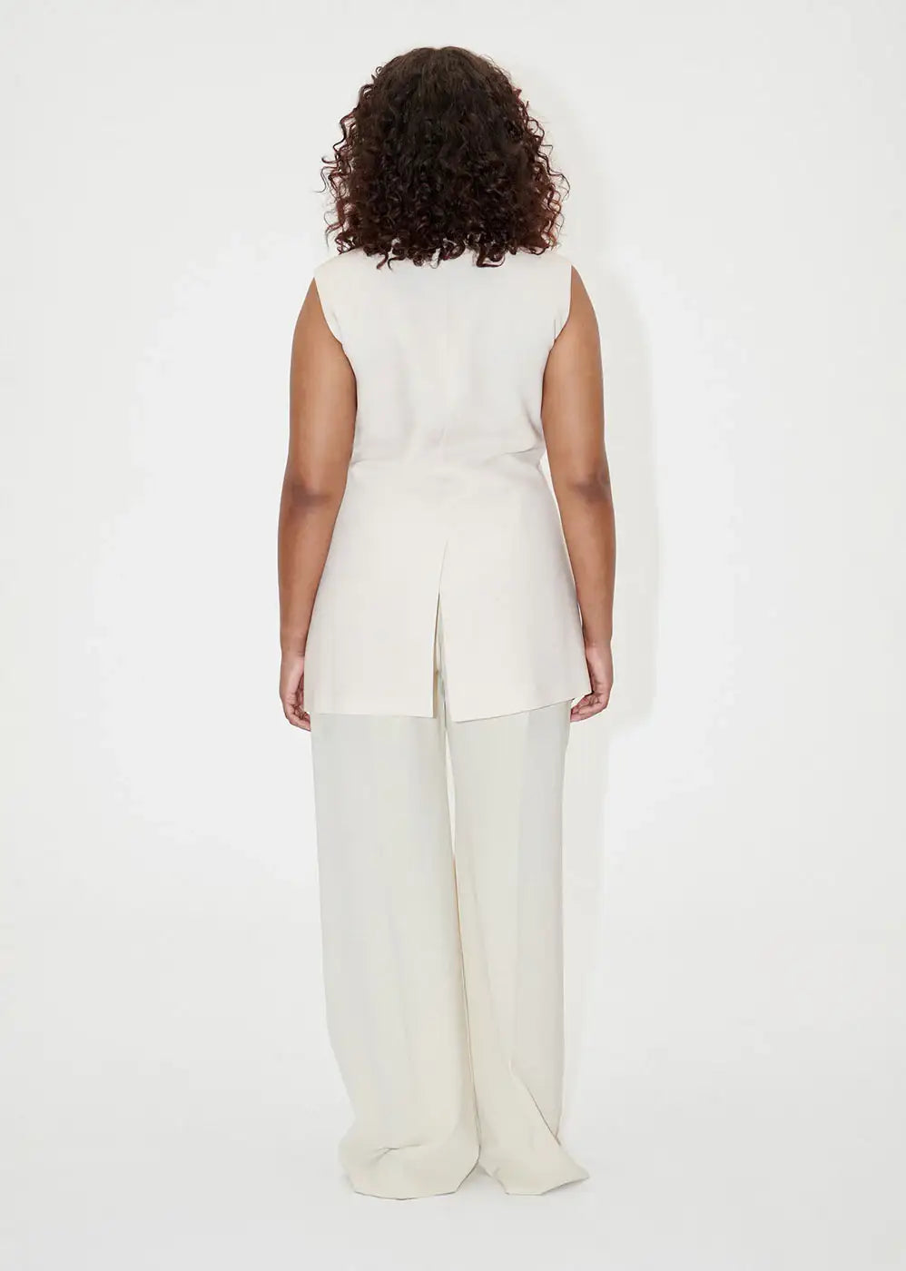 Back view of woman wearing ivory wide-leg dress pants and a sleeveless tunic, studio setting