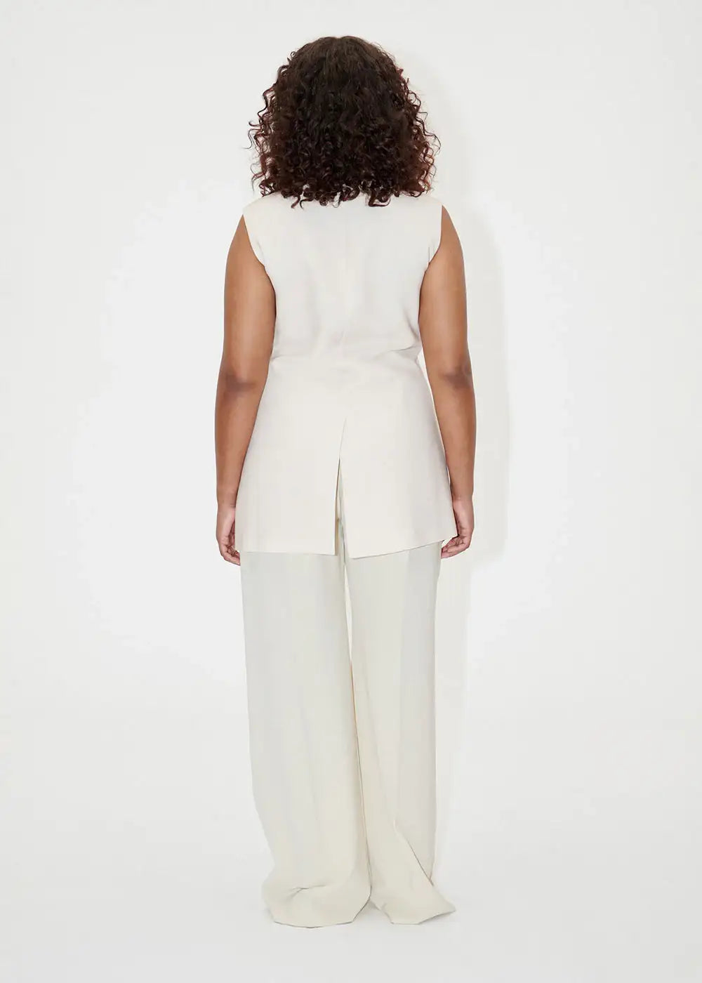 Back view of woman wearing ivory wide-leg dress pants and a sleeveless tunic, studio setting