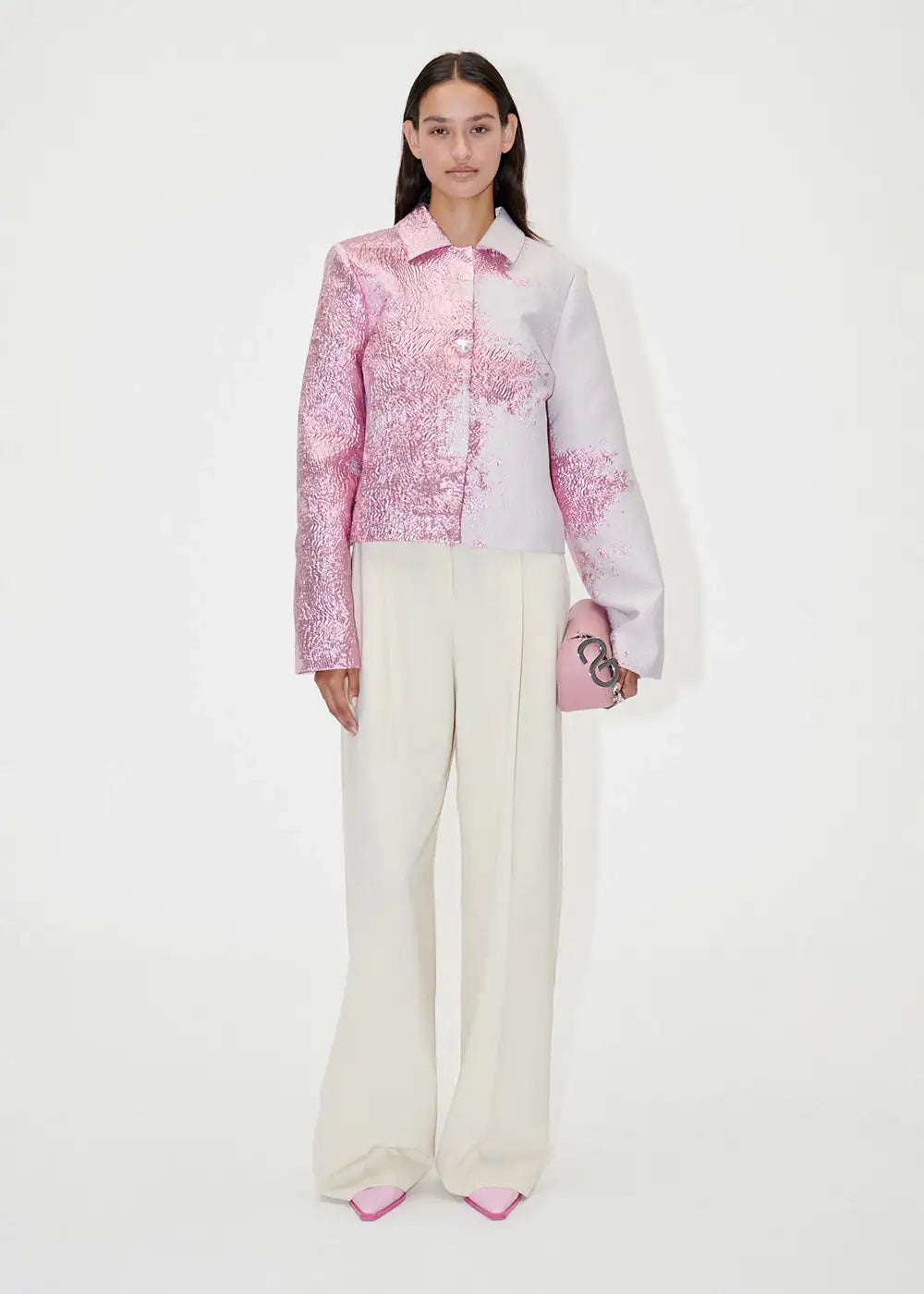 Woman in ivory wide-leg pants, metallic pink jacket, and pink heels holding a pink clutch