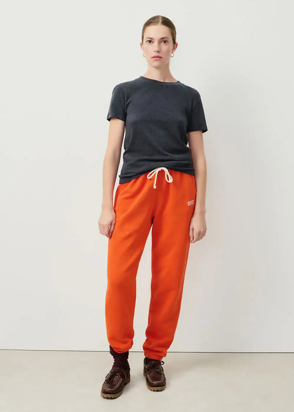 Woman wearing a dark grey t-shirt and orange drawstring sweatpants in minimalist setting
