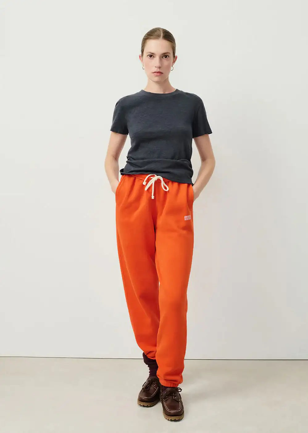 Woman wearing a dark grey t-shirt and bright orange jogger pants with drawstring waist