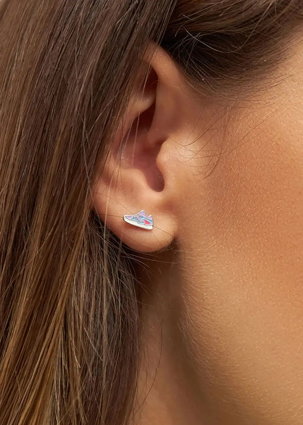 Close-up of a woman's ear wearing a silver sneaker-shaped stud earring
