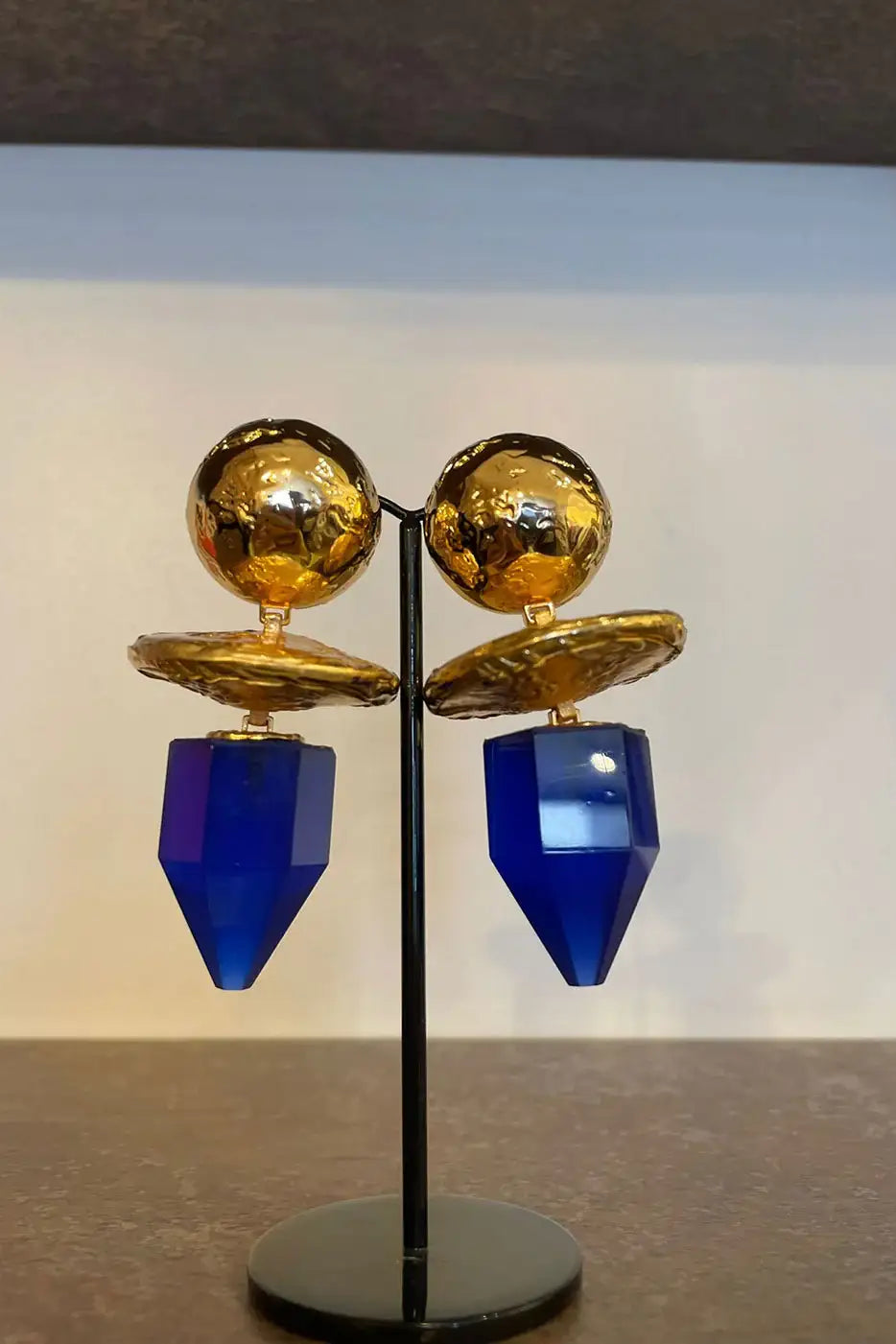 Gold and blue geometric statement earrings displayed on a stand, boutique jewelry