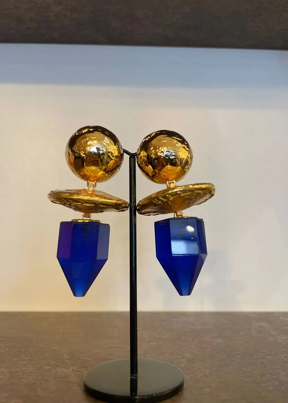 Gold and blue geometric statement earrings displayed on a stand, boutique jewelry