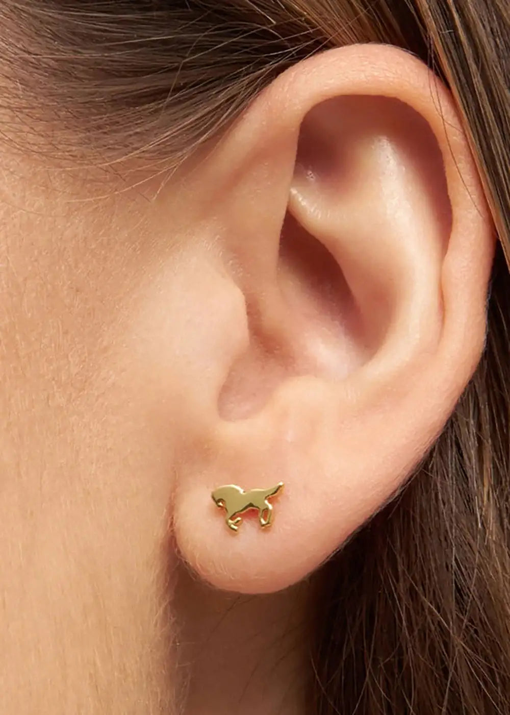 Gold plated horse shaped ear stud on woman's earlobe, minimalist jewelry