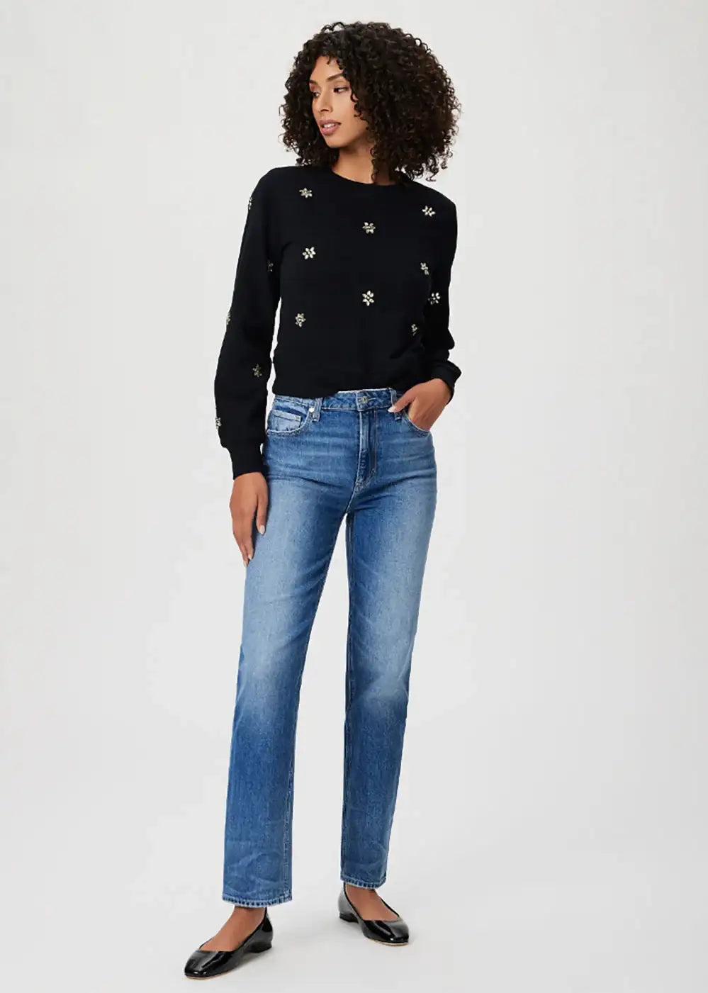 Woman wearing a black embellished sweater with blue straight-leg jeans and black flats