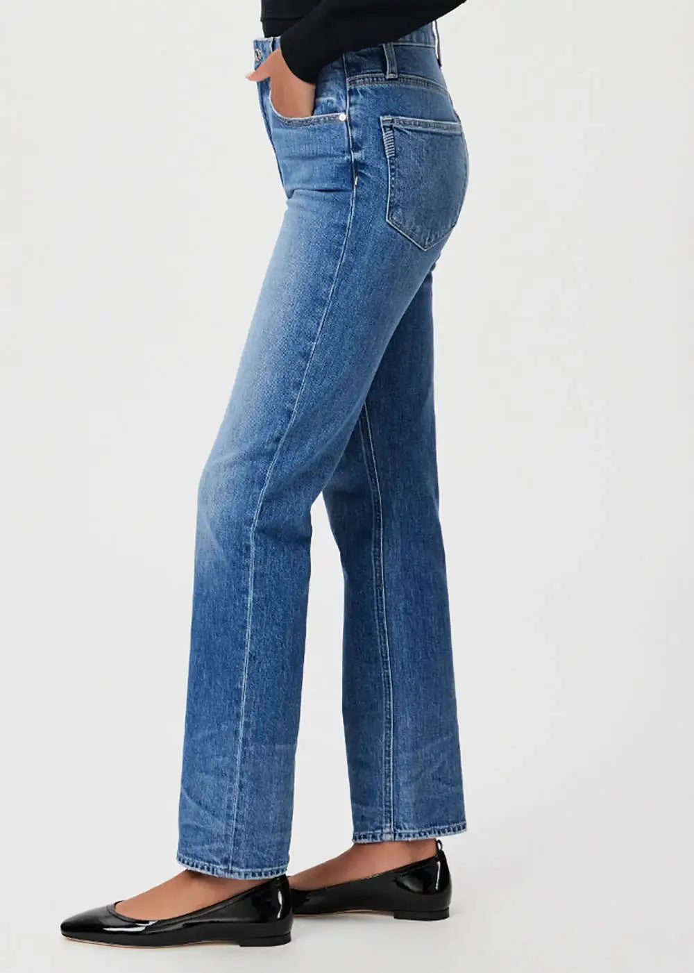 Woman wearing straight leg blue jeans and black flats on white background