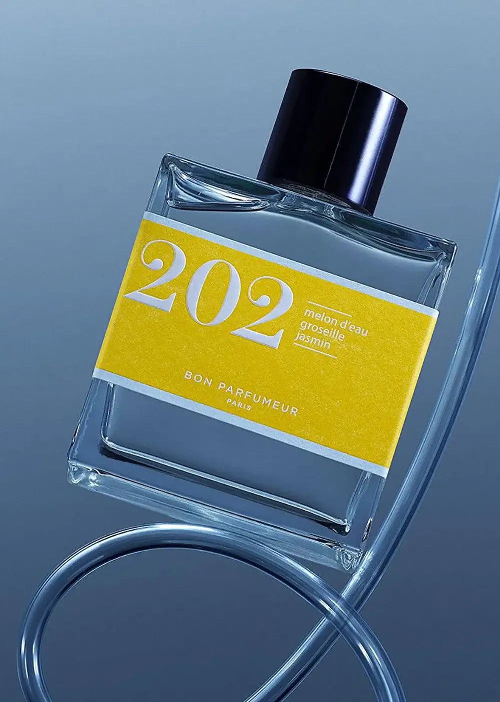 Glass perfume bottle with yellow label, black cap, and blue background