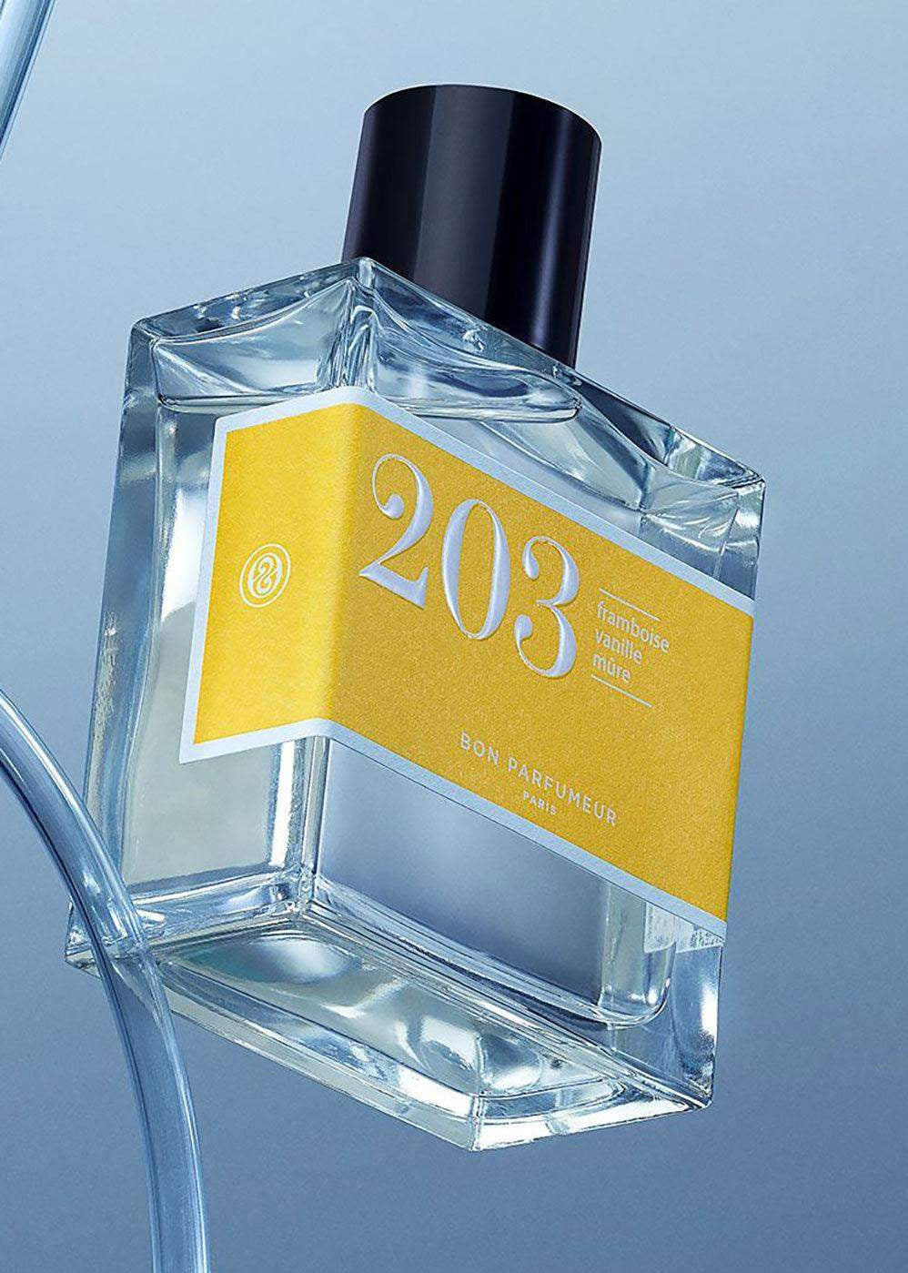 Clear glass perfume bottle with yellow label reading 203, black cap, blue background