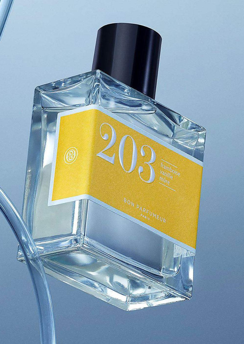 Clear glass perfume bottle with yellow label reading 203, black cap, blue background