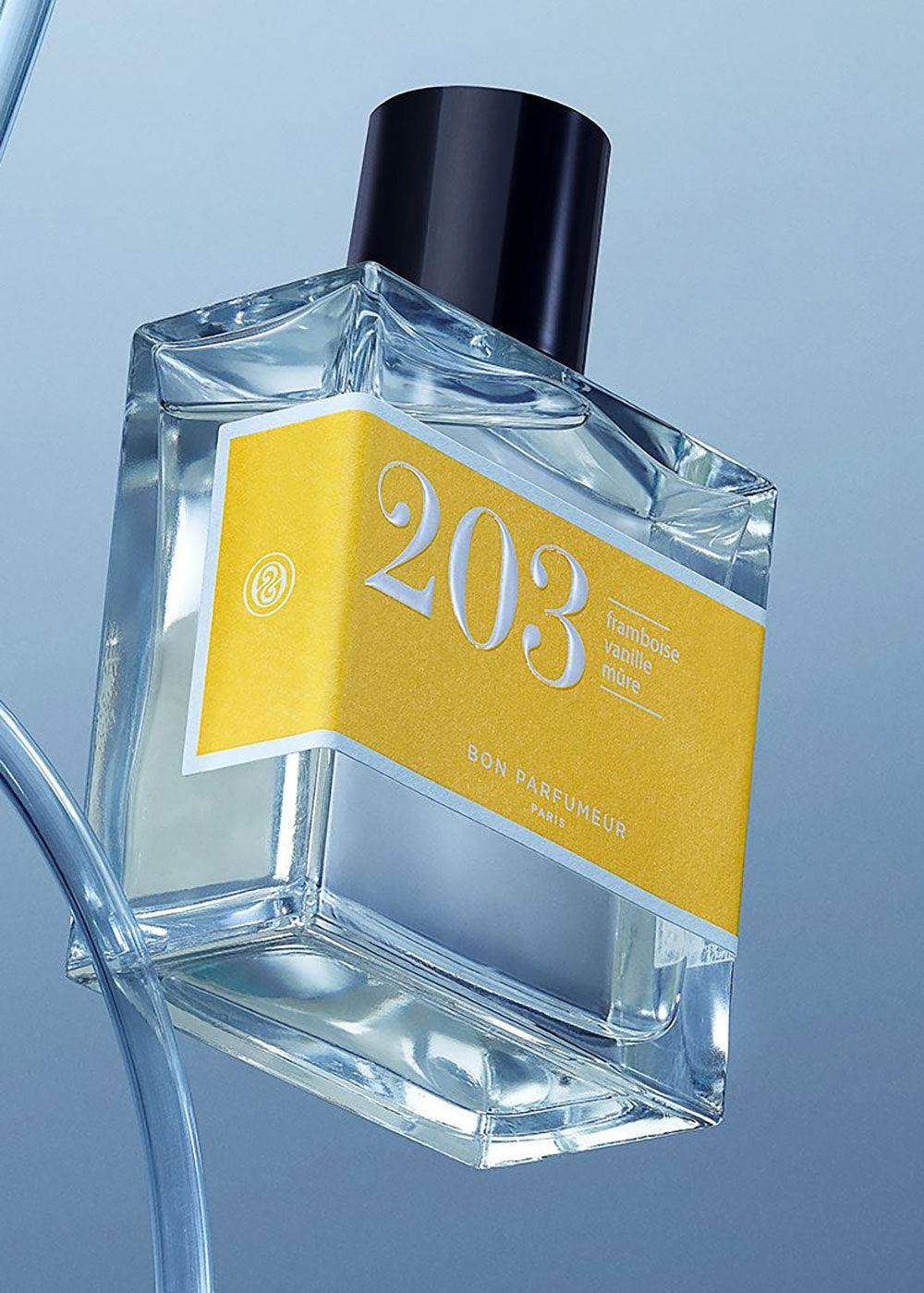 Clear glass perfume bottle with yellow label reading 203, black cap, blue background