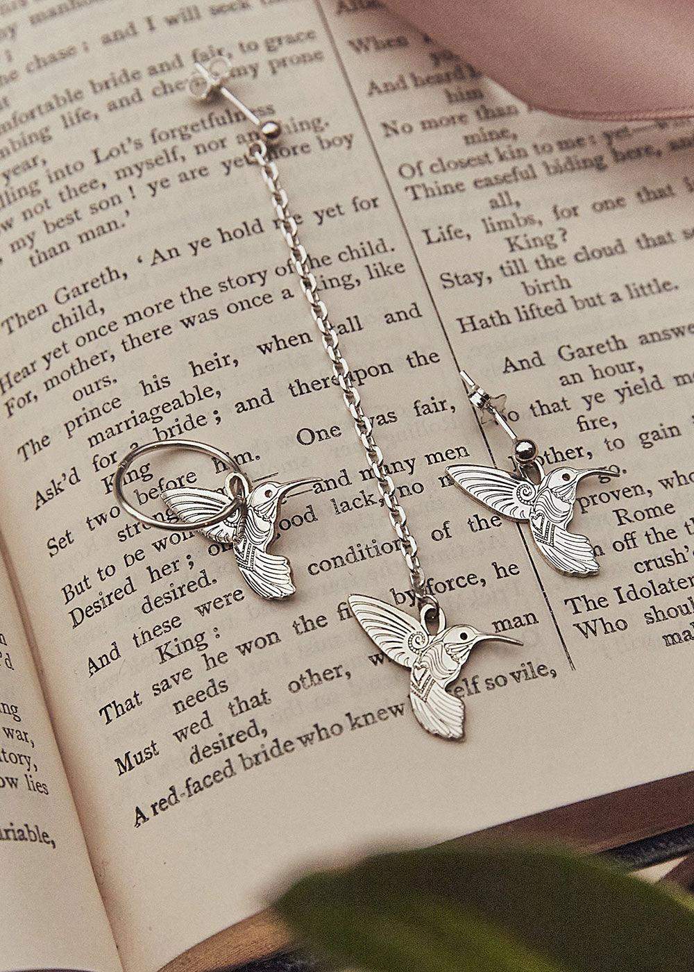 Silver hummingbird earrings and long drop earring displayed on an open book page.