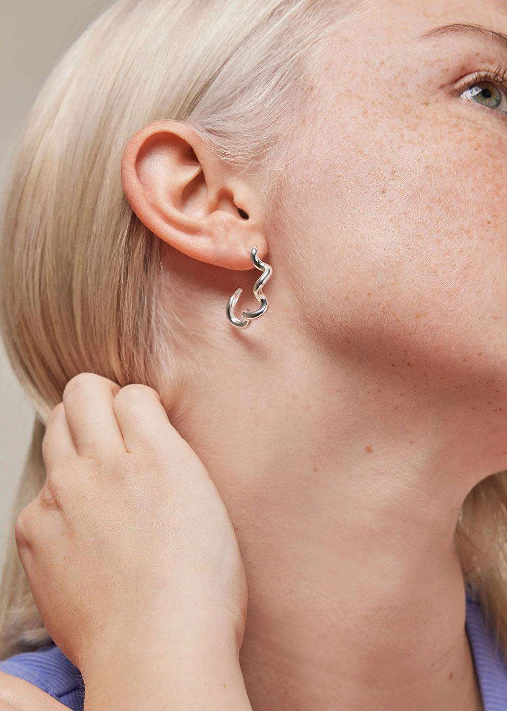 Curvy silver hoop earring worn on ear, contemporary jewelry style close-up