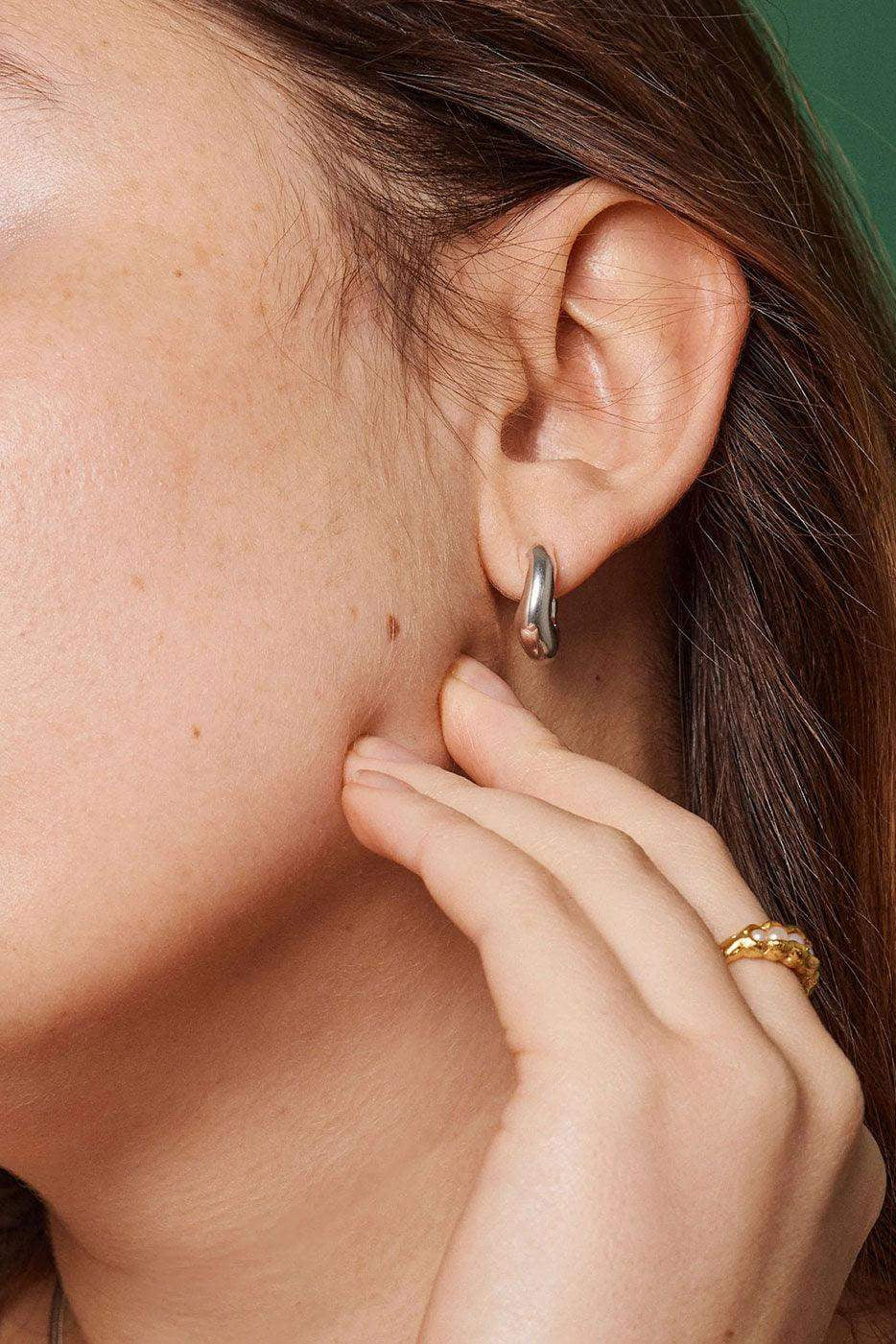 Silver Copenhagen Gianna hoop earring on ear, hand with gold ring visible