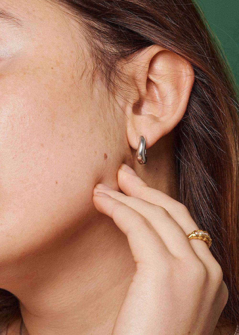 Silver Copenhagen Gianna hoop earring on ear, hand with gold ring visible