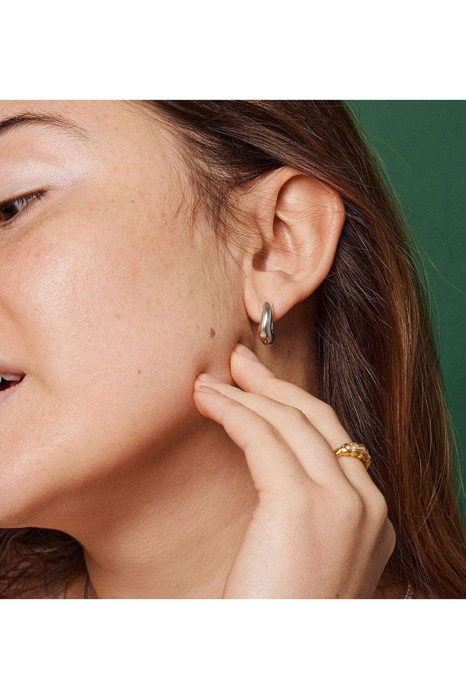 Close-up of woman wearing silver enamel hoop earring and gold braided ring