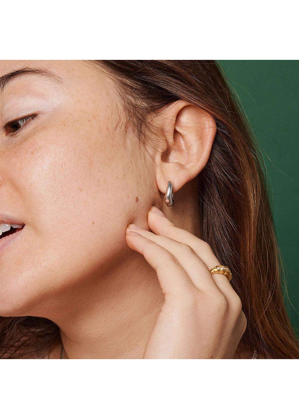 Close-up of woman wearing silver enamel hoop earring and gold braided ring